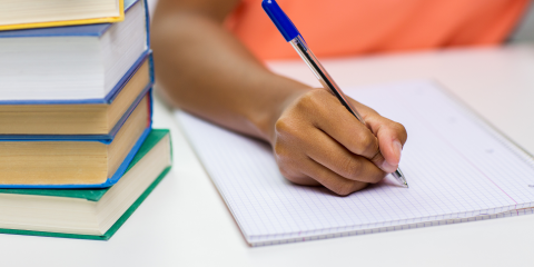 Woman in orange shirt writing in notebook next to stack of books