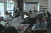 Video still of people gathered around a conference room table