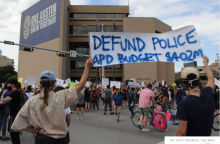 Protesters stand outside of the APD headquarters with a sign reading Defund police add budget $402M