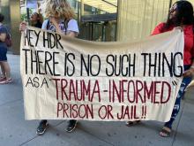 Protesters holding sign reading "hey HDR there is no such thing as a trauma-informed prison or jail"