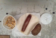 A hotdog with a tortilla, a cup of mush and a raw potato.