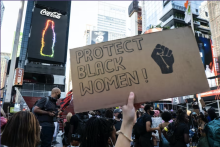 Hand of a person at a protest holding a sign reading protect Black women